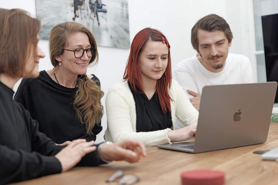 Wir suchen dich! Team chiliSCHARF sitzt gemeinsam vor dem MacBook und plant Marketingstrategien